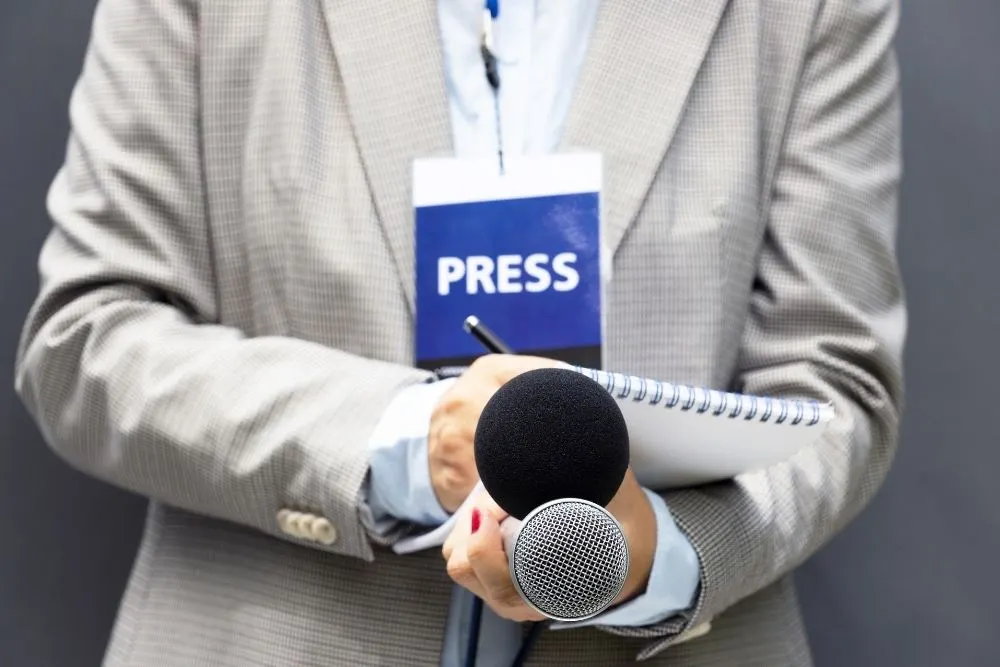 Jornalista a tirar notas num caderno com microfones na mão durante trabalho de assessoria de imprensa